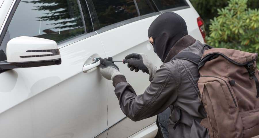 Thief trying to break into a white vehicle in a residential setting